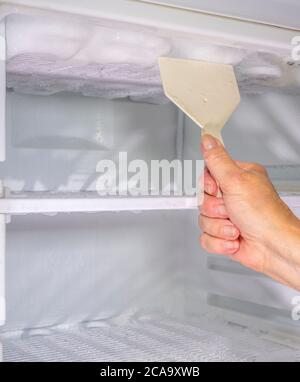 Nahaufnahme der Hand einer Frau mit einem flachen Kunststoffschaber auf der Innenseite einer heimischen Küche Gefrierschrank, um die Ansammlung von Eis und Frost zu entfernen. Stockfoto