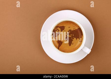 Nahaufnahme weiße Tasse auf Untertasse, voller Espresso-Kaffee mit Weltkarte auf Schaumkrema, auf Hintergrund braunes Papier mit Kopierfläche, erhöhte Ansicht von oben Stockfoto