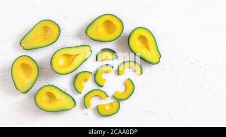 Top-Down-Ansicht, Avocado Hälfte und Scheiben, auf weißem Arbeitsbrett, Fruchtfleisch hat lebendige grüne und gelbe Farbe, Raum für Text rechts. Stockfoto