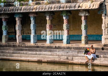 Mayiladuthurai, Tamil Nadu, Indien - Februar 2020: Ein älterer indischer Priester sitzt auf den Steinstufen eines heiligen Panzers im alten Hindu-Tempel Stockfoto