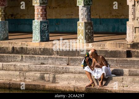 Mayiladuthurai, Tamil Nadu, Indien - Februar 2020: Ein älterer indischer Priester sitzt auf den Steinstufen eines heiligen Panzers im alten Hindu-Tempel Stockfoto