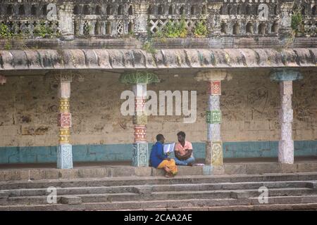 Mayiladuthurai, Tamil Nadu, Indien - Februar 2020: Zwei indische Männer sitzen neben den bunten, verzierten Steinsäulen des alten Hindu-Tempels von V. Stockfoto