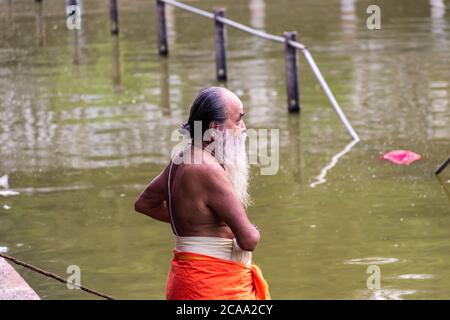 Mayiladuthurai, Tamil Nadu, Indien - Februar 2020: Ein älterer indischer Priester mit einem langen weißen Bart, gekleidet in einem Safran Lendenschurz im heiligen Tank von Stockfoto