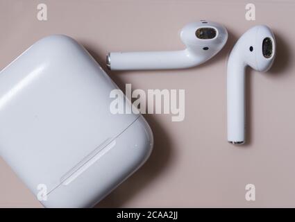 Schmutziger bluetooth-Kopfhörer auf einem goldrosa Hintergrund mit Gehäuse Stockfoto