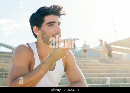 Schöner Sportler in einem Tank Top Aufnahme einer Sprachnachricht auf seinem Telefon nach seinem Sonnenuntergang Workout, Technologie und gesunde Lebensweise Konzept, Copy Space Stockfoto