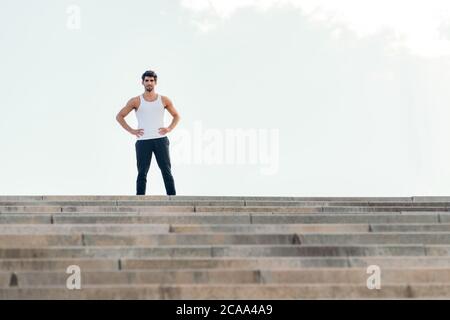 Ein gutaussehender Sportler, der mit den Händen auf der Hüfte oben auf einer Treppe steht, Konzept des urbanen Sports und des gesunden Lebensstils, Platz für Text kopieren Stockfoto