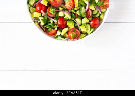 Salat aus frischen reifen Tomaten, Zwiebeln, Avocado, Gurke und Petersilie und Olivenöl, Salat auf weißem Teller auf weißem Holzhintergrund Stockfoto