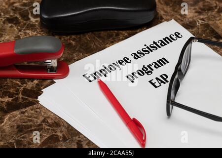 EAP-Programm zur Unterstützung von Mitarbeitern. Der Text ist auf weißem Papier geschrieben, neben einem roten Stift, einem Locheisen und einer Brille. Stockfoto
