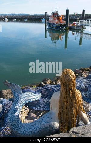 Früh AM BRIXHAM Hafenblick Figur der Meerjungfrau sitzend Felsbrocken Blick auf Rettungsboot Reflexionen in glattem Wasser klar Sky Hochformat Stockfoto