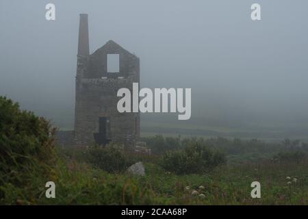 Ruinen der Carn Galver Cornwall Zinnmine im Nebel. Überreste von Bergwerksgebäuden und -Anlagen im Nebel Schrubben und Gräser im Vordergrund Landschaftsformat Stockfoto