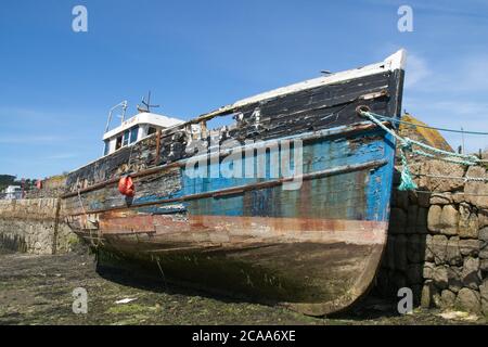 Verfallender Trawler jenseits der Reparatur und Verfall liegend an der Außenwand des Old Harbour Newlyn abblätternde Lackierung, verfaulender Holzrumpf. Querformat Stockfoto