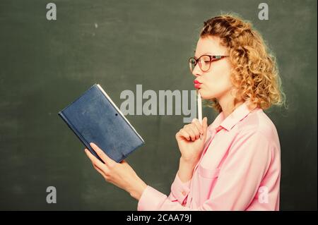 Frau Schullehrerin vor dem Schwarzen Brett. Leidenschaft für Wissen. Lehrer erklären hartes Thema. Lehrer bester Freund der Lernenden. Der Pädiater hält Buch und erklärt Informationen. Bildungskonzept. Stockfoto