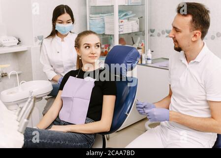 Zahnarzt im Gespräch mit einem Patienten. In der Nähe ist der Zahnarzthelfer. Empfang in der Zahnarztpraxis und zahnärztliche Behandlung. Stockfoto