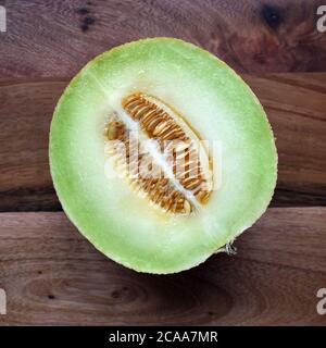 Frisches Galia Melone Obst halbiert Foto zeigt Samen und Fleisch auf einem Holzhintergrund unter natürlichem Licht. Appetitlich, ansprechend, einladendes Obst Stockfoto