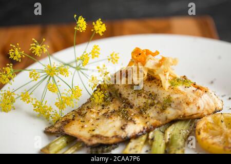 Ein Filet von wild, Linie gefangen Bass, Dicentrarchus labrax, gebraten in Butter, die auf einer Scheibe Fenchel serviert wurde und gewürzt mit Zitrone und Wild Stockfoto