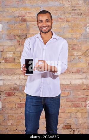 Ein hübscher junger Mann, der auf dem Bildschirm seines Smartphones in einem weißen Hemd. Stockfoto
