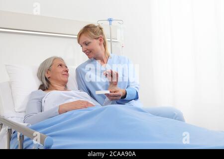 Krankenschwester gibt die Pille an die ältere Patientin im Bett des Krankenhauszimmers liegend, Konzept der Einsamkeit und Alterskrankheiten Stockfoto