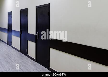 Leerer Korridor im modernen Bürogebäude. Entlang eines sehr langen Korridors mit beigefarbenen Wänden gibt es viele braune Türen. Stockfoto