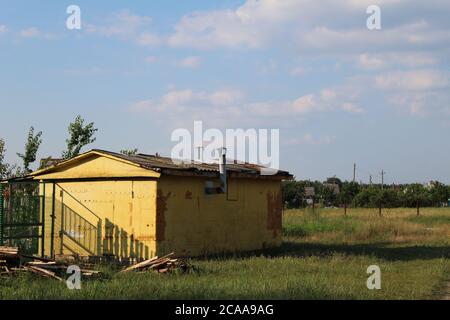 Gelbe Scheune Gebäude mit einem Kamin auf dem Hintergrund Eine Lichtung Wiese und blauen Himmel ländliche Landschaft Stockfoto