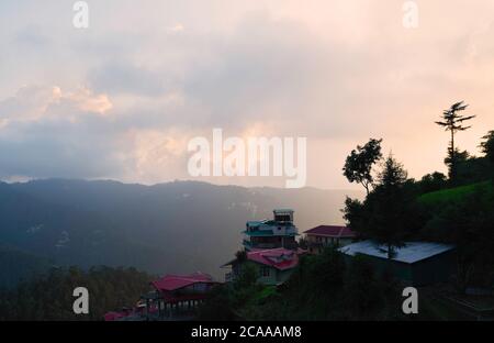 Sonnenuntergang über lokalen Haus und Dächern mit Blick auf Pinienwald und Himalaya-Berge unter bunten Himmel in Shimla, Himachal Pradesh, Indien. Stockfoto