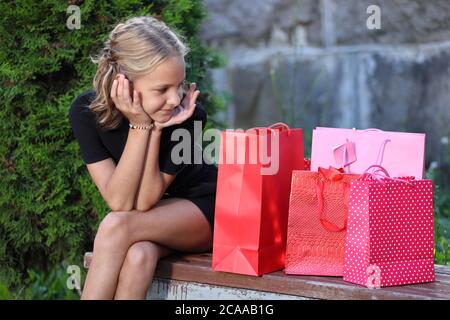 Girl in sitzt auf einer Parkbank mit farbigen Taschen Stockfoto