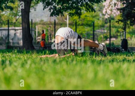 Junger sportlich schöner Mann, der Yoga im Park praktiziert und die Pflug-Pose macht. Stockfoto