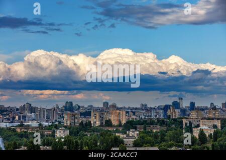 Sonnenstrahlen beleuchten die oberen Kappen weißer Wolken, die im Morgengrauen über der schlafenden Stadt hängen. Strahlendes Licht am dramatischen Morgenhimmel. Stockfoto