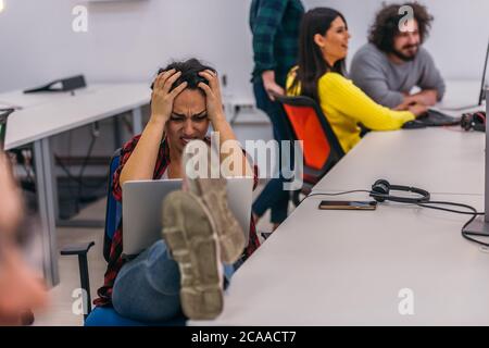 Eine nervöse Büroangestellte mit ihren Beinen auf ihrem Schreibtisch und ihrem Laptop in ihrem Schoß, die einen harten Tag hatten. Stockfoto