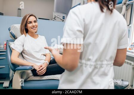 Freundliche Arzt Zahnarzt untersuchen Zähne der kaukasischen jungen Frau in Freizeitkleidung, isoliert in Zahnarztpraxis, mit speziellen medizinischen Geräten Stockfoto