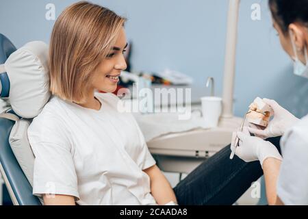 Junge kaukasische Frau Blick auf Prothese mit Interesse, Zahnarzt Arzt hält es und erklärt. Isoliert in der Zahnarztpraxis Stockfoto