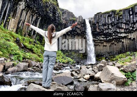 Island. Frau genießt majestätischen Svartifoss Wasserfall. Frau besucht berühmte Touristenattraktion von Island. Spektakuläres Naturdenkmal auf Stockfoto