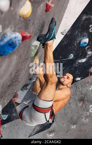 Muskulöse shitrless Mann Kletterwand mit Gerät belay an einem Indoor klettern. Kletterer üben Klettern in einer Kletterhalle. Stockfoto