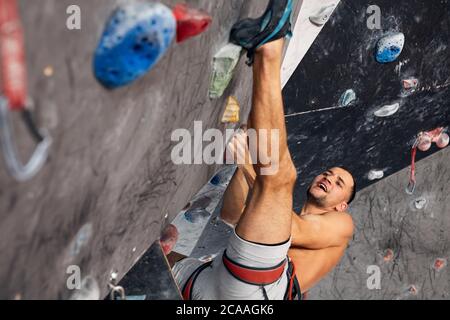 Blick von oben auf eine professionelle man Kletterer auf einem begehe Route paricipating in Wettbewerb, klettert auf den Kopf drinnen beim Bouldern Fitnessraum. Stockfoto