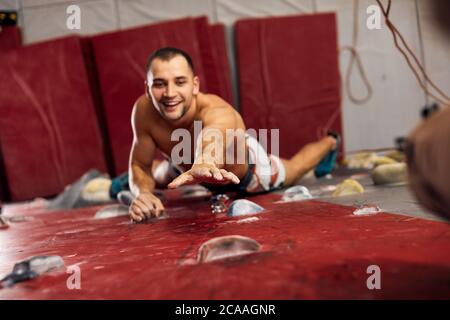 Sportlich glücklicher Geschäftsmann engagiert sich in seinem Hobby-Bouldern, Draufsicht. Ausgestattet mit einem Sicherungssystem männlichen Athleten Training in einer bunten Kletterhalle, schließen Stockfoto