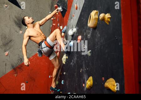 Nicht erkennbarer Athlet Kletterer Mann trainieren auf grauen praktischen Wand mit Fußrasten, Innenaufnahme, Nahaufnahme Bouldern, Rückansicht. Stockfoto