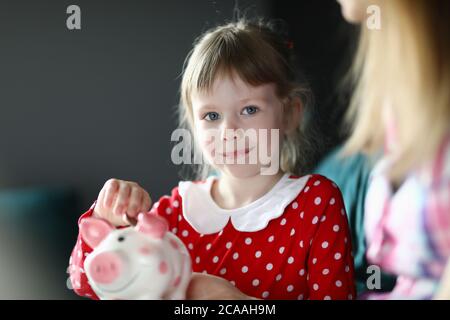 Glückliches kleines Mädchen legt Münzen in ein Sparschwein Stockfoto