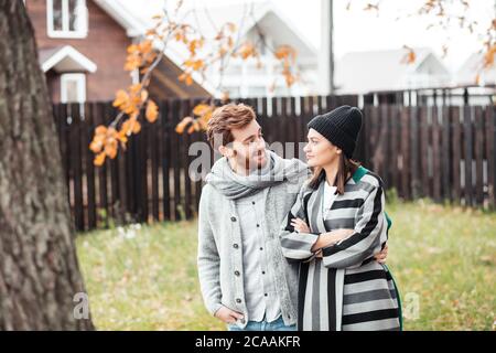 Glückliches junges Paar sitzt draußen, vor ihrem neuen Zuhause im Herbst warme Kleidung und träumt von ihrem spannenden Neukauf. Stockfoto