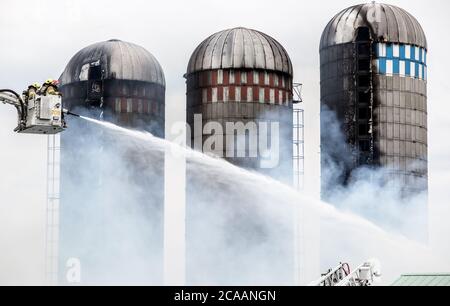 Feuerwehrleute kämpfen gegen Silofeuer. Sie sprühen Wasser aus dem Leiterkorb. Stockfoto