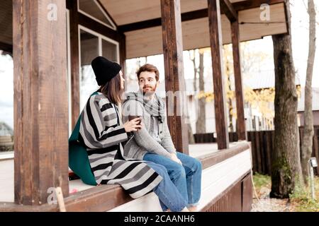 Glückliches junges Paar sitzt draußen, vor ihrem neuen Zuhause im Herbst warme Kleidung und träumt von ihrem spannenden Neukauf. Stockfoto