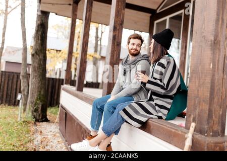 Glückliches junges Paar sitzt draußen, vor ihrem neuen Zuhause im Herbst warme Kleidung und träumt von ihrem spannenden Neukauf. Stockfoto