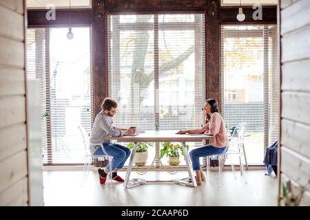 Panoramablick auf große geräumige Zimmer und kaukasischen Paar gegenüber am gleichen Tisch im Haus mit großen Fenstern im Hintergrund sitzen. Speicherplatz kopieren. Stockfoto