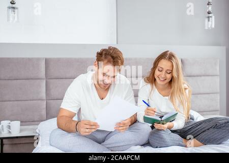 Positive Frau und Mann sitzen auf dem Bett und machen Pläne für den Urlaub. Nahaufnahme Foto. Familie, Beziehung, Liebe Konzept Stockfoto