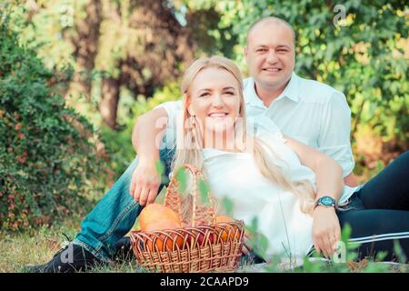 Aufgeregt erwachsenen Mann und Frau umarmen und Blick auf die Kamera, während auf grünem Gras im Park mit Obst Picknick sitzen Stockfoto