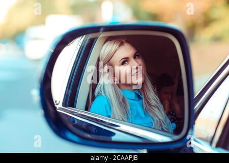 Blick durch den Autospiegel der schönen erwachsenen blonden Frau in blauem Hemd Blick auf Kamera, während drinnen sitzen Stockfoto