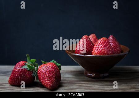 Einige Erdbeeren in einer Schüssel mit dunklem Hintergrund und Holztisch, dunkle Essensart mit Kopierplatz Stockfoto