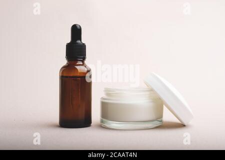 Serumglasflasche mit Pipette und Glas Gesichts- oder Körpercreme auf beigem Hintergrund. Natürliches organisches Spa Kosmetikkonzept. Vorderansicht. Platz für Ihre Stockfoto