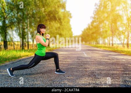 Junge Frau, die sich die Beine vor dem Joggen auf Asphaltstraße in der Landschaft streckt Stockfoto