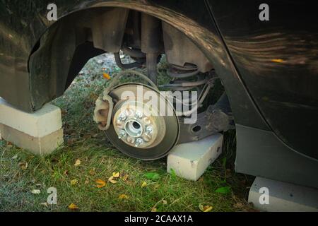 Nahaufnahme des Autos auf Ziegelsteinen draußen. Konzept der gestohlenen Fahrzeugeräder. Auto mit fehlendem Rad. Stockfoto