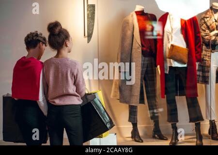Zwei kaukasische Frauen mit Einkaufstaschen, die vor der Boutique der Frauenkollektion stehen, Rückansicht. Ein Schaufenster von Kleidung Shop, zeigen weiblichen Mantel Stockfoto