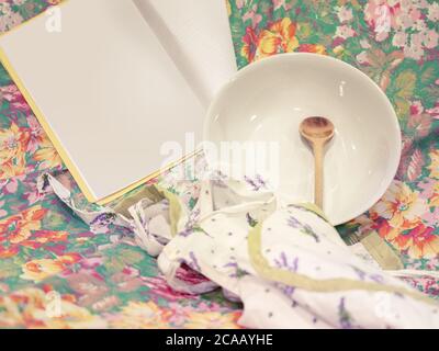Leerer Teller auf geblümtem Hintergrund, Hunger, Holzlöffel, Kochen, Papier für Rezepte Stockfoto